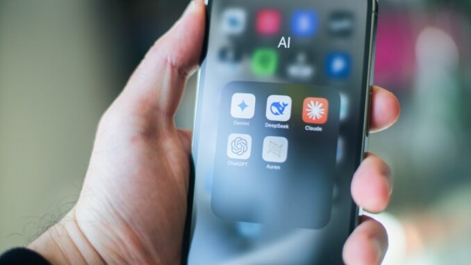 A hand holds a smartphone with various apps.